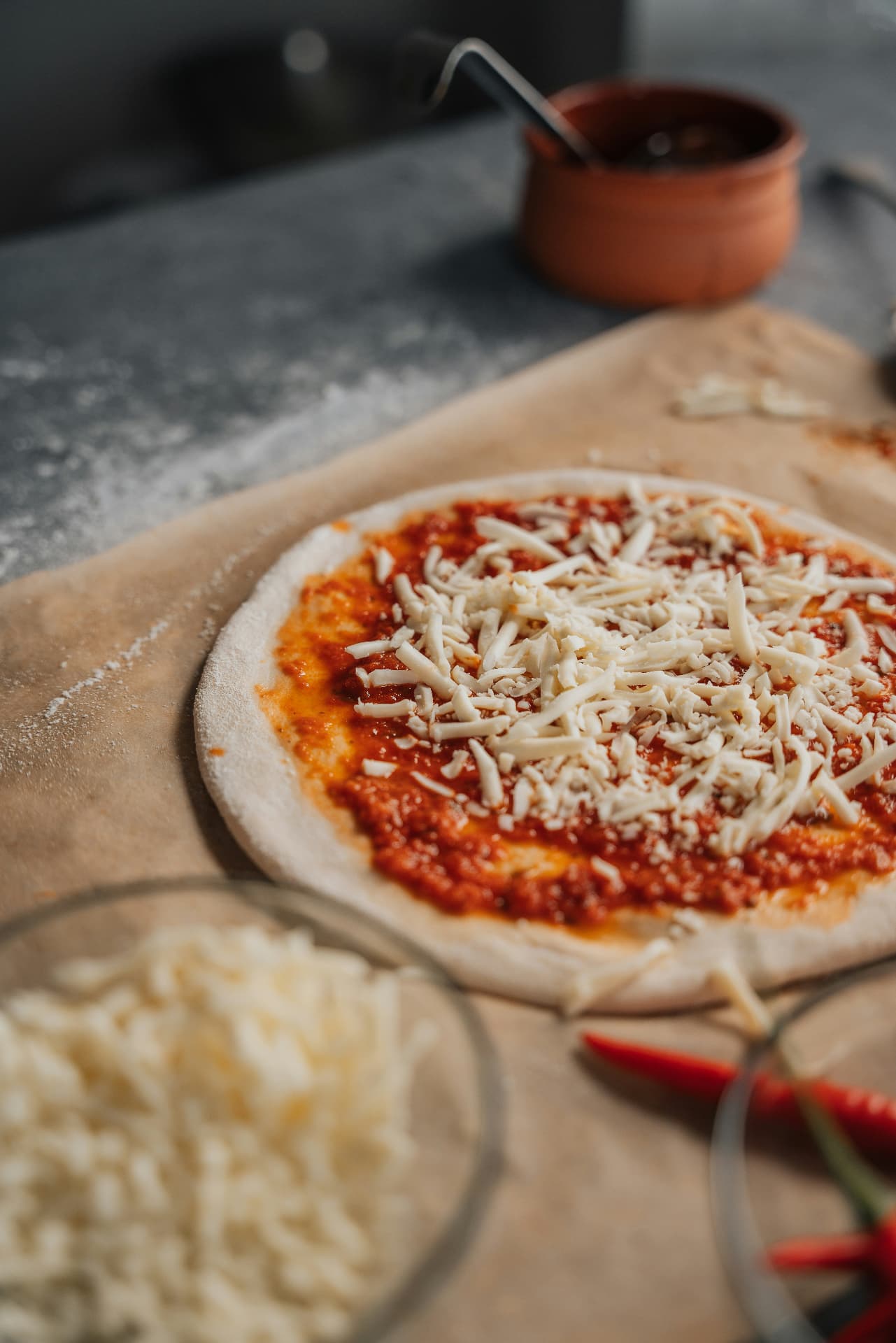 An uncooked pizza on parchment paper, spread with tomato sauce and topped with shredded mozzarella, on a floured counter